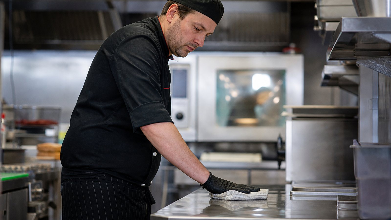 Cuisinier désinfectant un plan de travail en inox dans une cuisine professionnelle